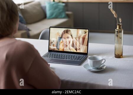 Vue arrière de la femme âgée assise à la table avant de l'ordinateur portable et de parler à sa petite-fille en ligne à accueil Banque D'Images