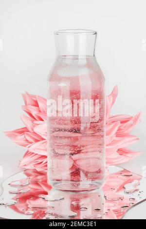 fleurs roses déformées par l'eau dans la bouteille avec miroir sur fond bleu. eau pure, relax, surréaliste, concept de maison écologique. espace copie Banque D'Images