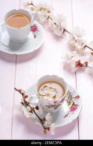 Branches d'Apricot en fleur et deux tasses en porcelaine avec thé et sur une table en bois rose clair. Banque D'Images