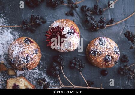 muffin aux raisins de corinthe sur fond sombre à côté des baies sur les branches. et un bouquet de fleurs. dans un style rustique. style sombre Banque D'Images