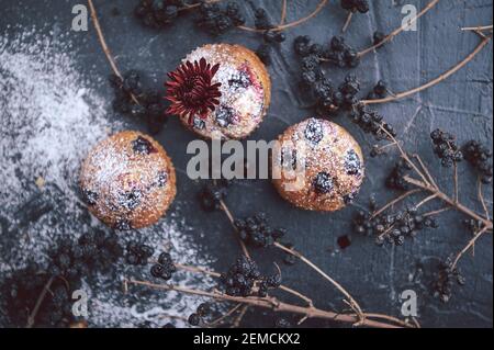 muffin aux raisins de corinthe sur fond sombre à côté des baies sur les branches. et un bouquet de fleurs. dans un style rustique. style sombre Banque D'Images