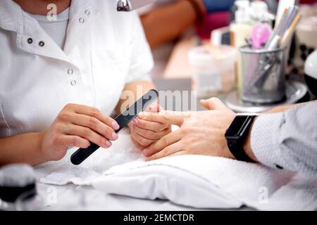 Lime à ongles de planche d'émeri dans les mains d'un manucuriste qualifié, manucure pour hommes Banque D'Images