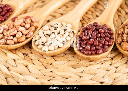 Différents haricots dans les cuillères en bois sur fond beige. Banque D'Images