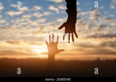 Silhouette de la portée, donnant une main d'aide, l'espoir et le soutien l'un l'autre sur fond de coucher de soleil. Concept d'aide Banque D'Images