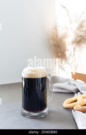 Bière artisanale foncée dans une grande tasse à bière et délicieux maison bretzels sur fond gris Banque D'Images