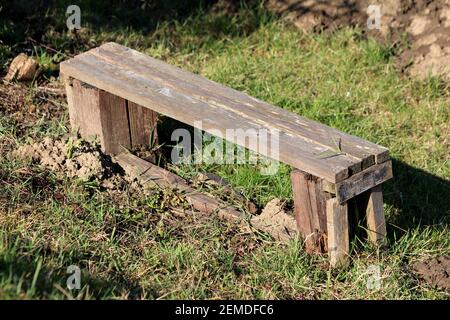 Improvisé maison craqué panneaux en bois délabrés petit banc laissé dans le jardin de la maison urbaine est entouré d'herbe et de sol sec hiver chaud et ensoleillé Banque D'Images