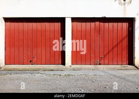 Vieux portes de garage doubles en métal rouge foncé avec des pièces rouillées et petites poignées de porte montées sur garage blanc fissuré délabré mur du bâtiment Banque D'Images
