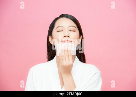 Gros plan de beau modèle de fille asiatique heureuse avec maquillage naturel en utilisant des feuilles absorbantes d'huile, produit de beauté au studio Banque D'Images