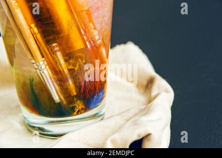 Brosses artistiques souillées dans la peinture trempez dans un verre avec eau Banque D'Images