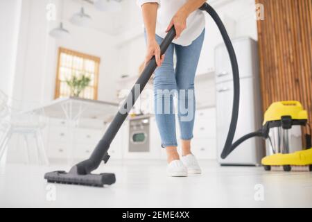 Femme passant l'aspirateur dans la cuisine blanche l'après-midi Banque D'Images