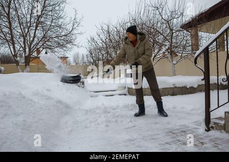 l'homme jette de la neige de la cour avant de sa propre maison avec une pelle en plastique après une forte chute de neige. Banque D'Images