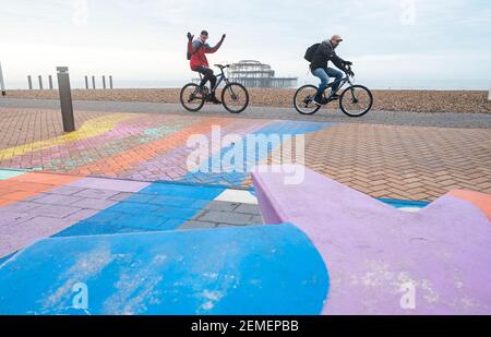 Brighton Royaume-Uni 25 février 2021 - les cyclistes heureux passent par la jetée ouest de Brighton sur une matinée calme et sombre le long de la côte du Sussex, mais le temps ensoleillé est prévu pour les prochains jours : Credit Simon Dack / Alamy Live News Banque D'Images