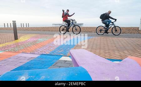 Brighton Royaume-Uni 25 février 2021 - les cyclistes heureux passent par la jetée ouest de Brighton sur une matinée calme et sombre le long de la côte du Sussex, mais le temps ensoleillé est prévu pour les prochains jours : Credit Simon Dack / Alamy Live News Banque D'Images