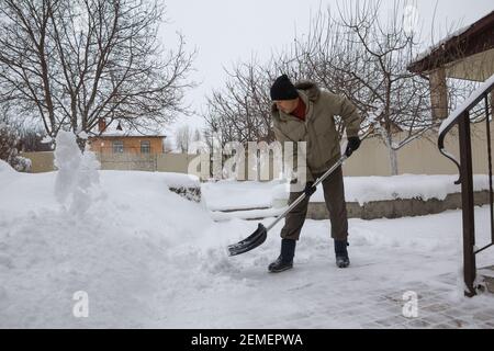 l'homme jette de la neige de la cour avant de sa propre maison avec une pelle en plastique après une forte chute de neige. Banque D'Images