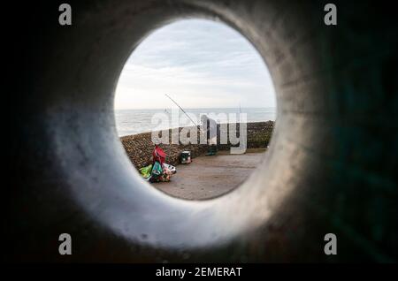 Brighton Royaume-Uni 25 février 2021 - UN pêcheur sur le front de mer de Brighton pendant une matinée sombre et nuageux le long de la côte du Sussex, mais le temps ensoleillé est prévu pour les prochains jours : Credit Simon Dack / Alamy Live News Banque D'Images