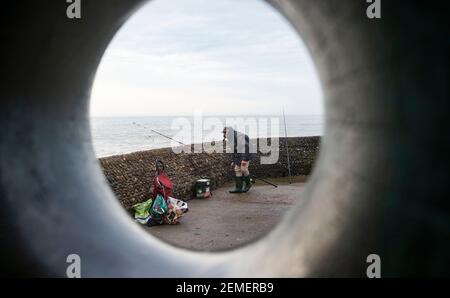 Brighton Royaume-Uni 25 février 2021 - UN pêcheur sur le front de mer de Brighton pendant une matinée sombre et nuageux le long de la côte du Sussex, mais le temps ensoleillé est prévu pour les prochains jours : Credit Simon Dack / Alamy Live News Banque D'Images