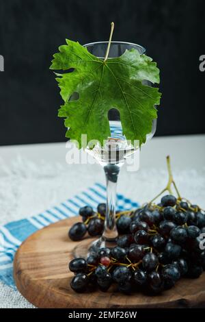 Un bouquet de raisins noirs et un verre de vin avec feuille sur table blanche Banque D'Images