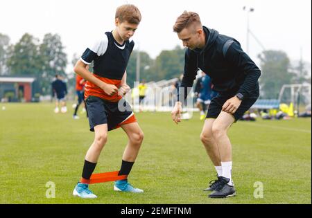 Entraîneur de football avec jeune joueur. Garçon sur le terrain de football s'étirant sur un tapis d'exercice. Entraîneur masculin et entraîneur personnel donnant des conseils au jeune athlète Banque D'Images