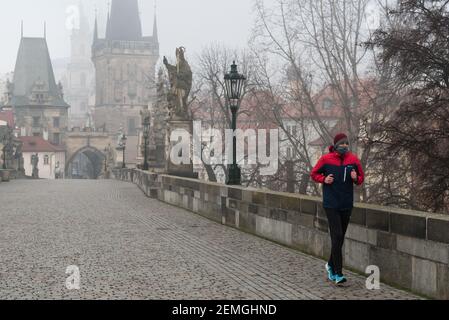 Prague, République tchèque. 25 février 2021. Un coureur portant un masque facial comme mesure préventive contre la propagation du coronavirus court le long d'un pont Charles vide à Prague pendant une matinée brumeuse. A partir d'aujourd'hui, le port d'un masque FFP2 est obligatoire dans les magasins et les transports publics en République tchèque. Crédit : SOPA Images Limited/Alamy Live News Banque D'Images