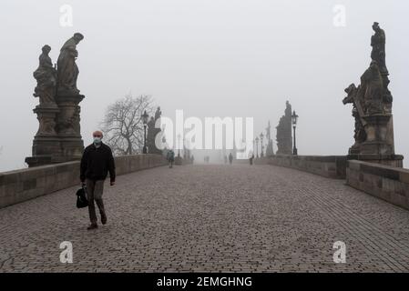 Prague, République tchèque. 25 février 2021. Un homme portant un masque facial comme mesure préventive contre la propagation du coronavirus marche le long d'un pont Charles vide à Prague pendant une matinée brumeuse. A partir d'aujourd'hui, le port d'un masque FFP2 est obligatoire dans les magasins et les transports publics en République tchèque. Crédit : SOPA Images Limited/Alamy Live News Banque D'Images