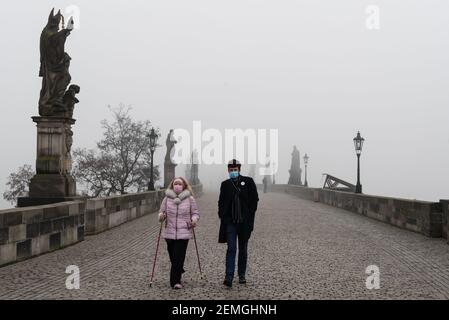 Prague, République tchèque. 25 février 2021. Un couple portant un masque facial comme mesure préventive contre la propagation du coronavirus marche le long d'un pont Charles vide à Prague pendant une matinée brumeuse. A partir d'aujourd'hui, le port d'un masque FFP2 est obligatoire dans les magasins et les transports publics en République tchèque. Crédit : SOPA Images Limited/Alamy Live News Banque D'Images