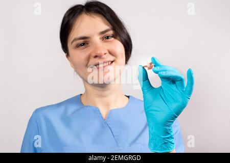 Dentiste tenant une fausse dent artificielle en céramique. Prothèse dentaire dans les mains gantées du médecin en gros plan. Photo conceptuelle de la dentisterie. Banque D'Images