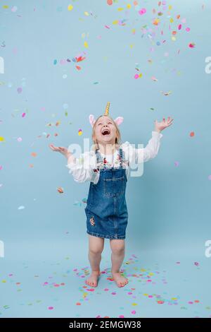 Heureuse petite fille dans le groupe de tête unicorn clatant ses mains sur fond bleu Banque D'Images