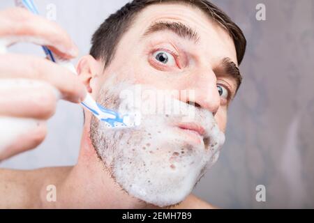 Homme avec visage drôle de rasage de près dans la salle de bains à la maison. Banque D'Images
