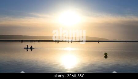 Deux personnes s'agenouillent sur une planche à aubes en pagayant le long du lac marin West Kirby pendant le coucher du soleil en février 2021. Banque D'Images