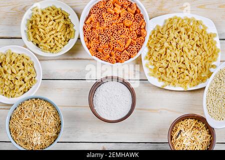 Vue de dessus de diverses pâtes crues sur blanc et bois bols avec farine Banque D'Images