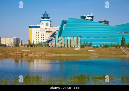 Kazakhstan, Astana, la ville se reflète dans la rivière Isahim, en regardant vers la salle de concert centrale et l'hôtel Beijing Palace Soluxe Banque D'Images