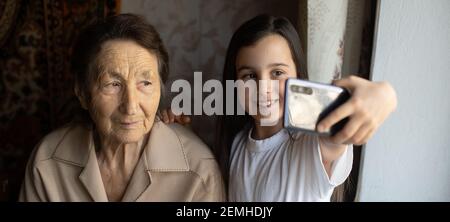 La grande-grand-mère est assise avec la grande-petite-fille et regarde dans le smartphone. Grand-mère et enfant prennent un selfie sur un smartphone. Grand-mère avec Banque D'Images