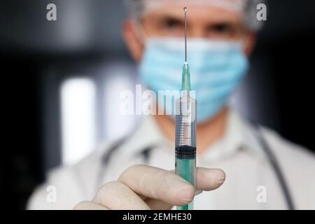 Seringue dans la main du médecin, homme dans un masque médical et gants de protection se préparant à l'injection. Concept de vaccination pendant la pandémie de Covid-19 Banque D'Images