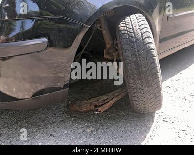 Roue endommagée d'une voiture causée par un trou dans une route rurale. Roue arrachée d'essieu corrodée sur la voiture. Banque D'Images