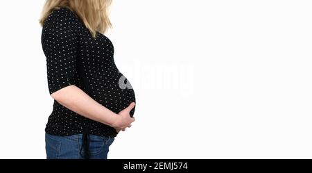 vue latérale de la section médiane de la femme enceinte de 9 mois chemise à pois et jean avec les mains sur le ventre arrière-plan blanc Banque D'Images