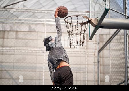 jeune homme asiatique adulte joueur de basket-ball essayant une dunk sur un terrain extérieur Banque D'Images