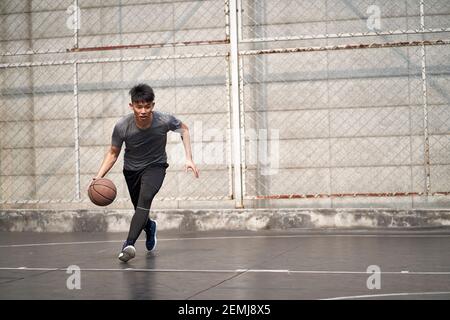 un jeune homme asiatique essaie de jouer un dunk sur un terrain extérieur Banque D'Images