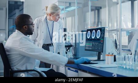 Laboratoire de recherche médicale moderne : deux scientifiques utilisent un ordinateur avec écran montrant des images IRM du cerveau, les spécialistes discutent de la technologie innovante Banque D'Images