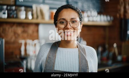 Le magnifique Barista féminin latino-américain avec des cheveux courts et des lunettes projette un sourire heureux dans le café-restaurant bar. Portrait d'un employé heureux derrière Banque D'Images