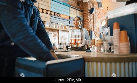 Magnifique Happy Latin Barista sert commande d'un courrier de livraison de nourriture et passe le porte-gobelet en carton avec deux cafés à emporter. L'expert de la livraison met Banque D'Images