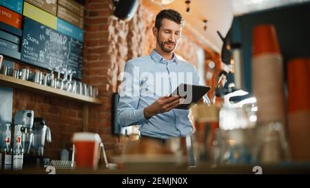 Beau caucasien propriétaire de café travaille sur l'ordinateur tablette et de vérifier l'inventaire dans un confortable café de style loft. Directeur de restaurant réussi Banque D'Images