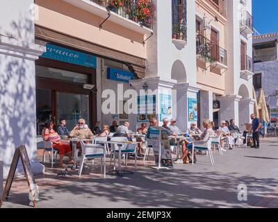 Les touristes, certains portant des masques faciaux, s'assoient dans un bar avec terrasse ensoleillée à Nerja, Malaga, Espagne Banque D'Images