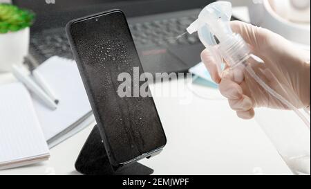Femme en gants utilise un spray antiseptique pour nettoyer l'espace de travail de smartphomeon. Désinfection phomeand ordinateur portable clavier par alcool désinfectant par femme dans Banque D'Images