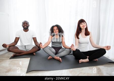 Calme et santé parents multiraciaux enseignant la méditation avec la mignonne fille de race mixte sur le tapis de yoga. Conscient heureux parents et enfant fille faisant yoga ex Banque D'Images