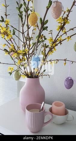 vase couleur pastel avec des oeufs de forsythia et de pâques et un tasse de café rose Banque D'Images