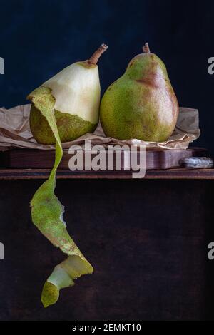 Deux belles poires de conférence sur un sac en papier, une poire coupée ouverte avec la pelure pendante, fond noir, espace de copie Banque D'Images