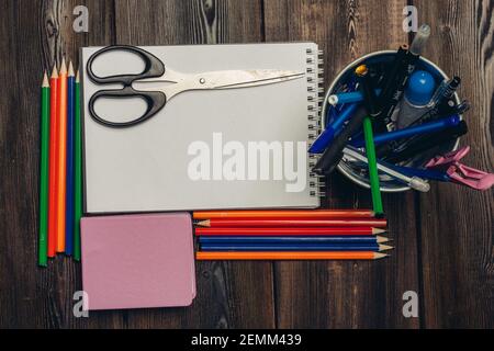 des ciseaux sont couillés sur un carnet ouvert et des crayons de couleur vue sur une table en bois Banque D'Images