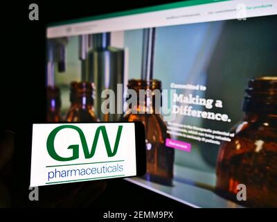 Personne tenant un smartphone avec le logo de la société britannique GW Pharmaceuticals PLC à l'écran en face du site Web. Mise au point sur l'affichage du téléphone. Photo non modifiée. Banque D'Images