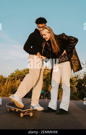 Amis hommes et femmes debout près du skateboard dans le parc pendant coucher de soleil Banque D'Images