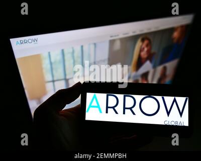 Personne tenant un smartphone avec le logo de la société d'investissement britannique Arrow Global Group PLC à l'écran devant le site Web. Mise au point sur l'affichage du téléphone. Banque D'Images